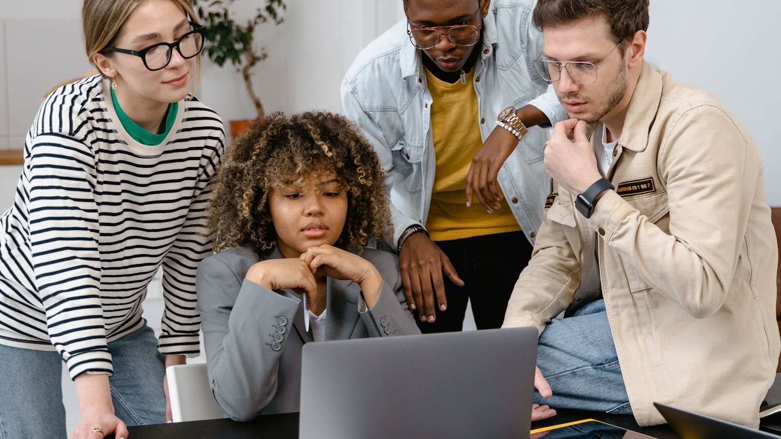 A group in discussion around a laptop during a serious hiring conversation