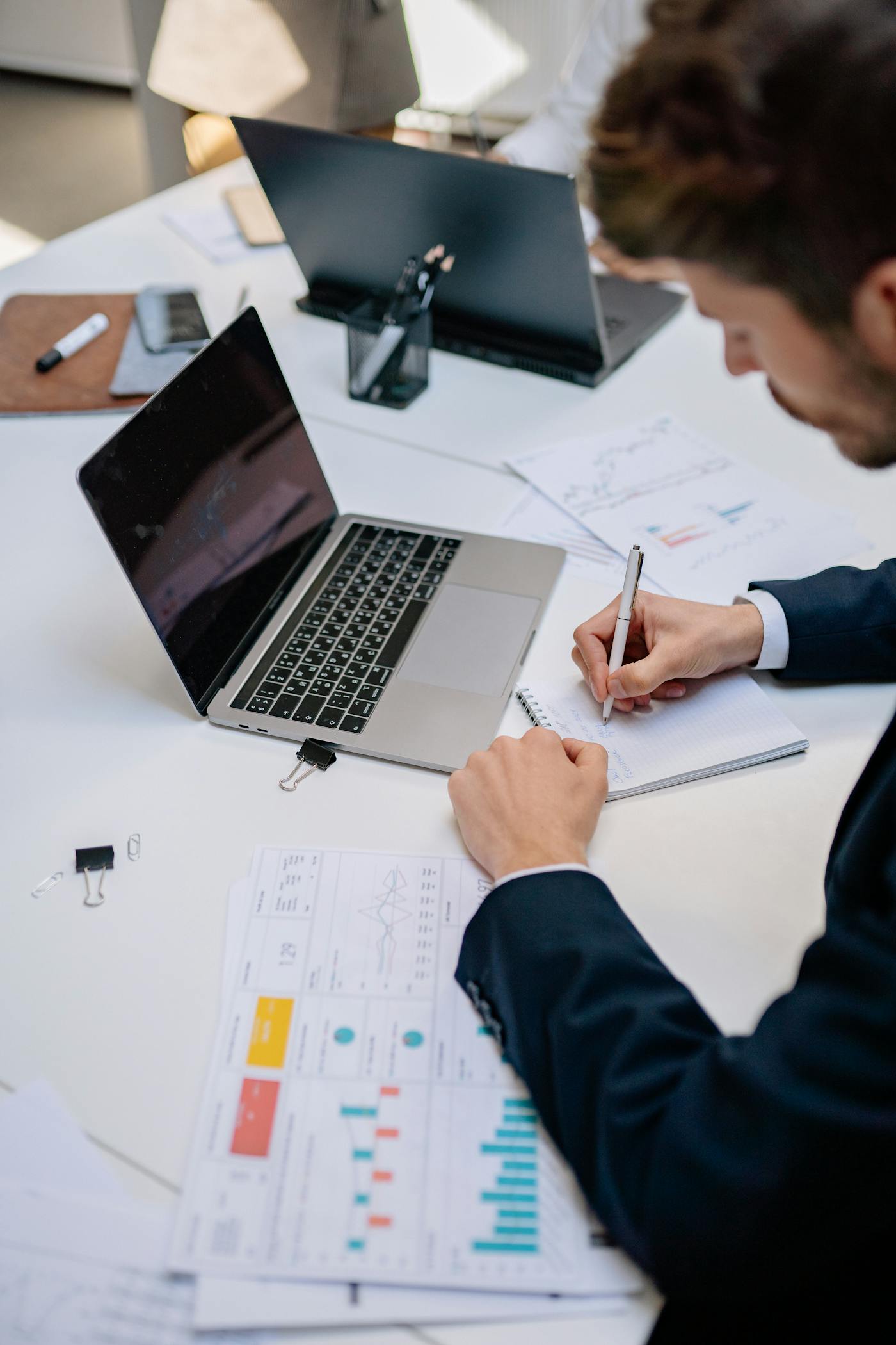 A professional taking notes beside a laptop and documents during digital planning